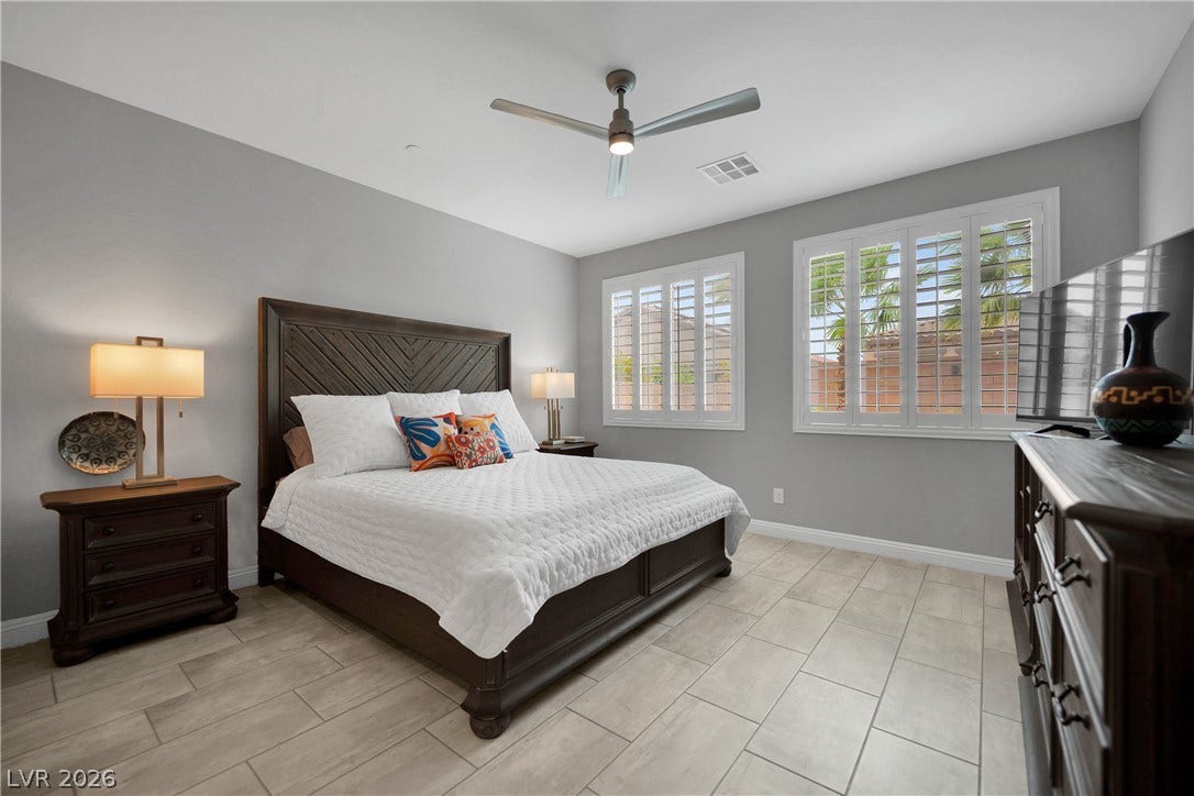 Relax in this well-lit bedroom featuring a ceiling fan, plantation shutters, and stylish tile flooring.
