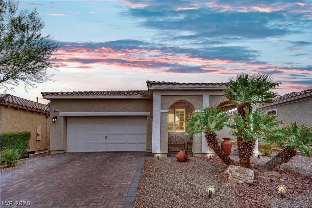 A terracotta-tiled roof crowns this residence with a paved driveway, desert landscaping, and prominent palm trees under a dramatic sky.