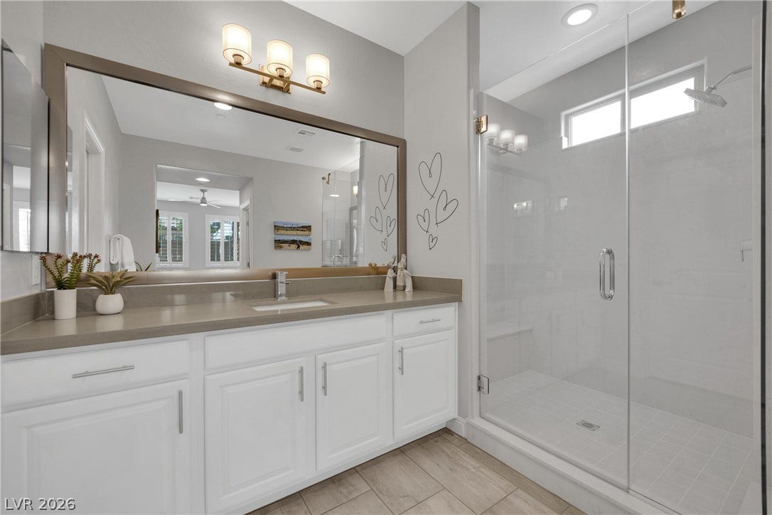 A well-lit primary bathroom featuring a spacious vanity, sleek gray countertops, and a modern glass-enclosed shower.