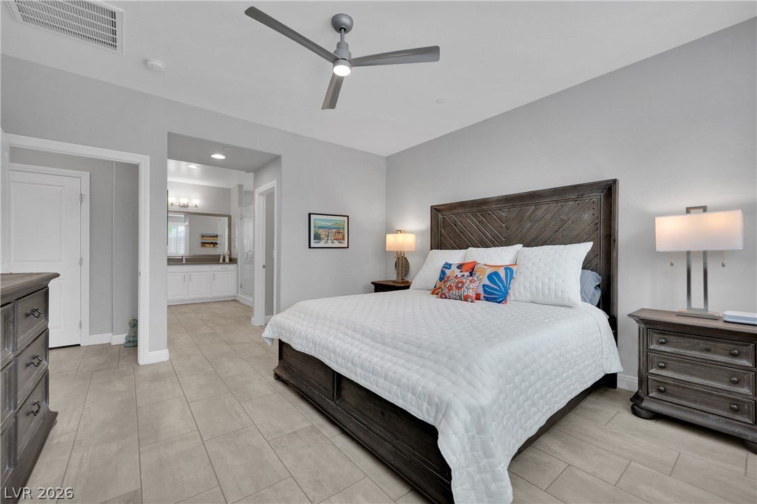Relax in a generously proportioned bedroom featuring a stylish ceiling fan and durable tile flooring, with an adjoining bathroom vanity.