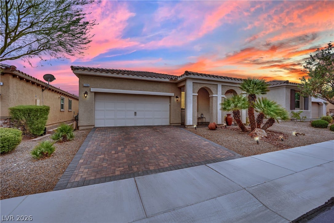 Spanish-inspired home with a paver driveway, archways, and vibrant landscaping under a painted sunset sky.