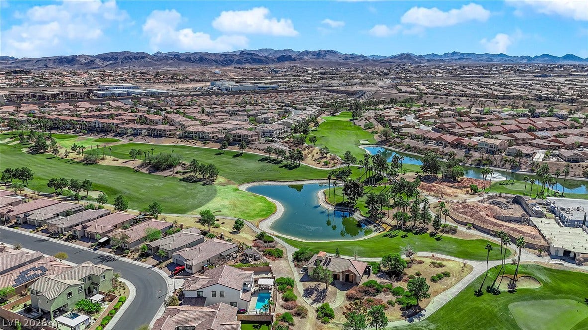 An aerial panorama showcases a master-planned community with lush golf courses, serene water features, and expansive mountain vistas.