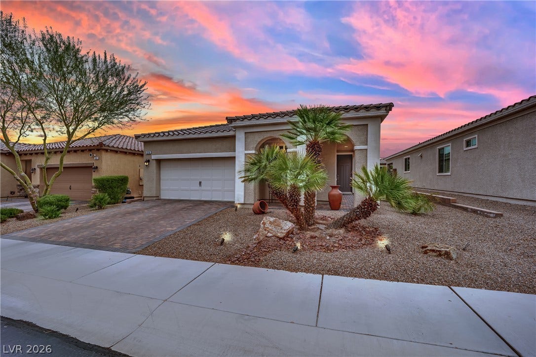 An inviting front facade features a tile roof, paved driveway, and desert landscaping under a vibrant sunset.