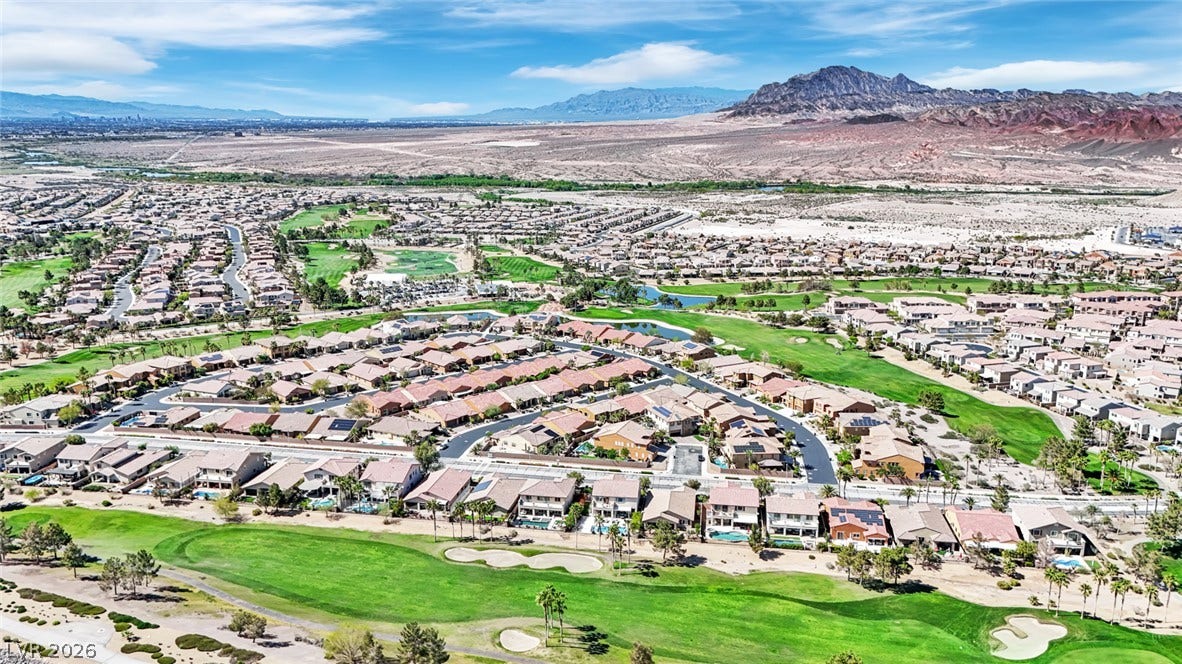 An aerial perspective reveals a vibrant golf course community nestled against a distant mountain range and expansive desert landscape.