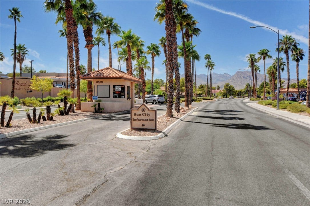 2621 Hanging Rock Drive, Las Vegas, NV 89134 Palm trees frame the paved entry street leading past a guardhouse toward distant mountain peaks.