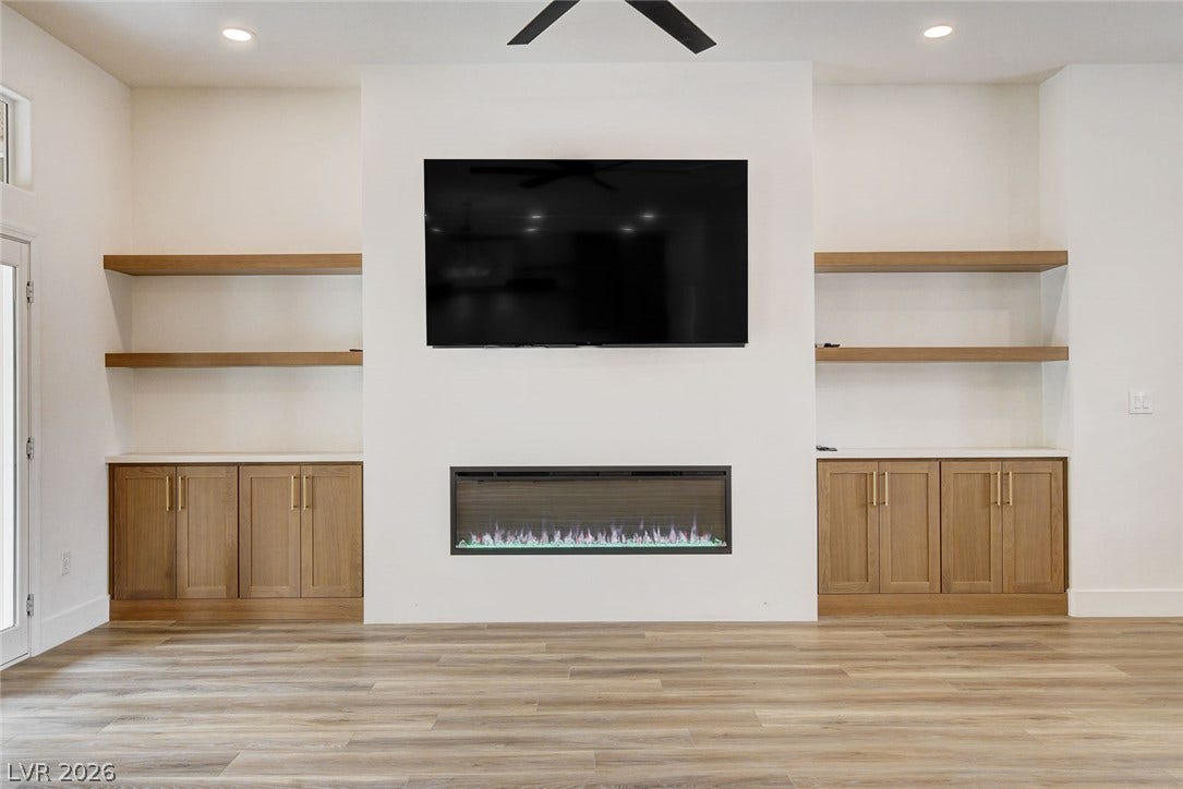 2621 Hanging Rock Drive, Las Vegas, NV 89134 A modern fireplace is flanked by built-in shelving and cabinets over rich wood flooring.