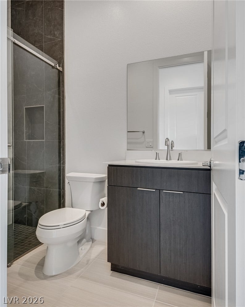 10226 Pleasant Knoll Avenue, Las Vegas, NV 89166 A modern bathroom features a dark vanity, sleek tile flooring, and a glass-enclosed walk-in shower.