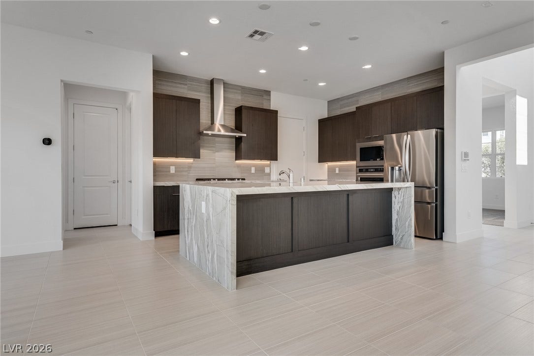 10226 Pleasant Knoll Avenue, Las Vegas, NV 89166 An expansive kitchen features high-end cabinetry, a waterfall stone island, and sleek tile flooring.