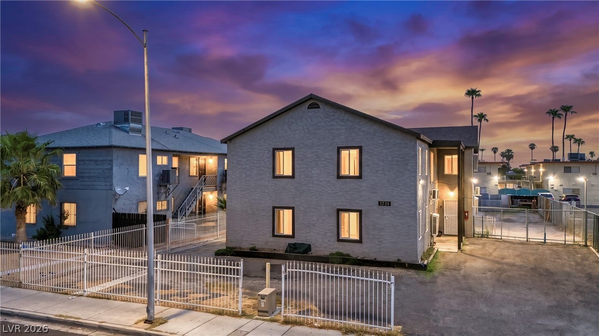 Multi-family residential buildings sit secured behind clean fencing under a dramatic sunset sky.