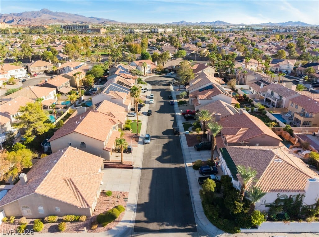 Sun-drenched tile roofs line a quiet suburban street set against a majestic mountain backdrop.