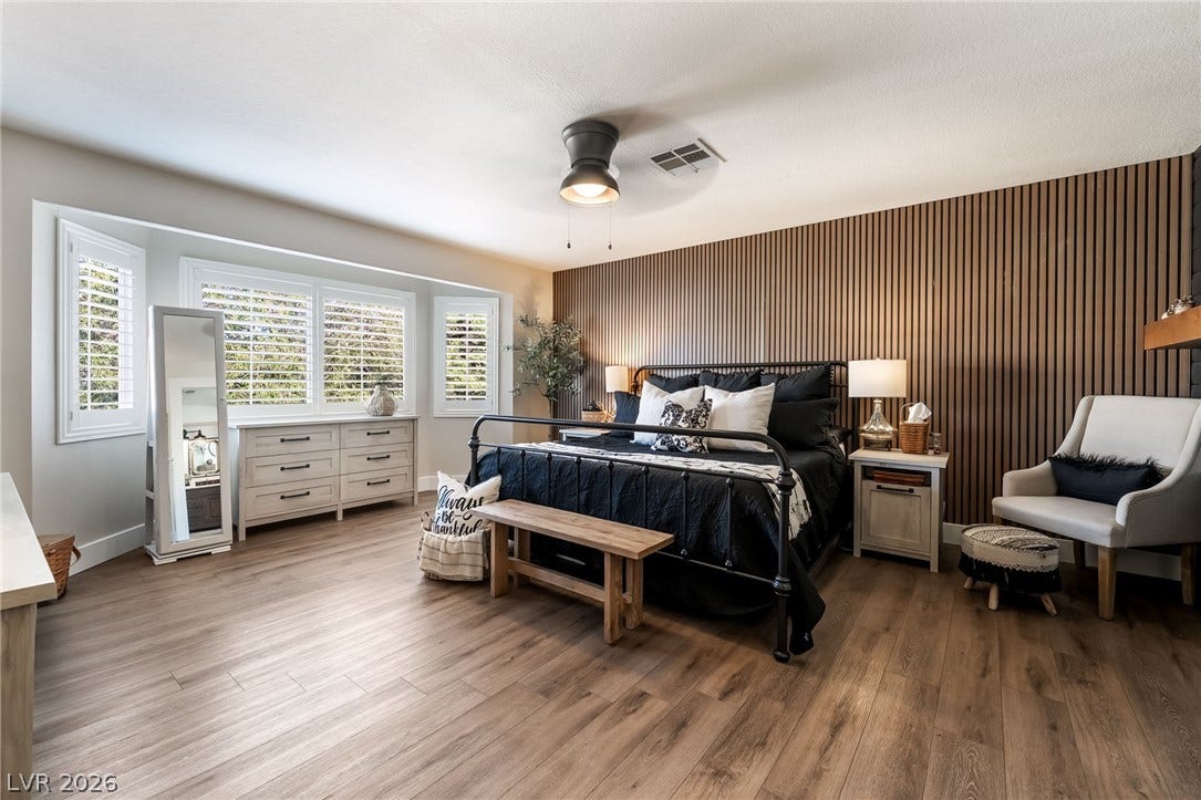 Rich wood plank flooring and a custom wood-paneled wall define this comfortable main bedroom.