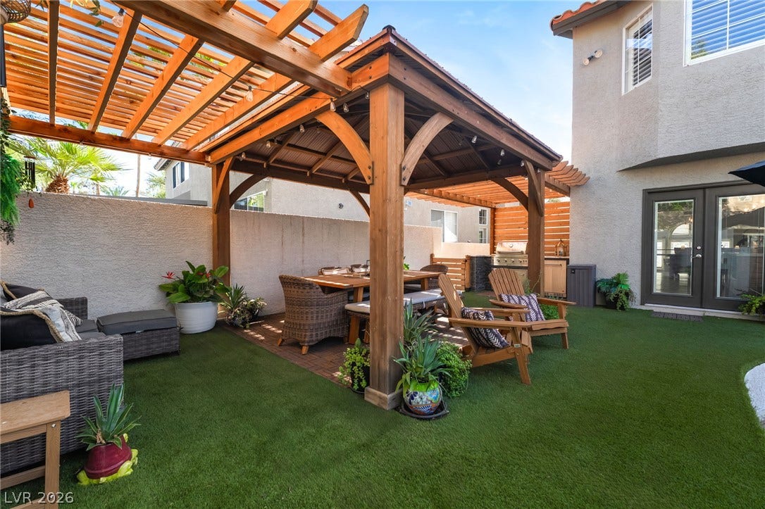 A spacious outdoor living area features a wooden pavilion and integrated kitchen adjacent to the home.