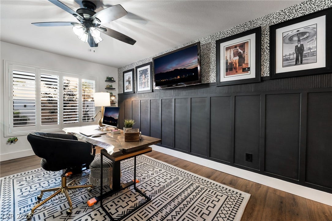 Board and batten wainscoting details this study featuring wood flooring and built-in plantation shutters.