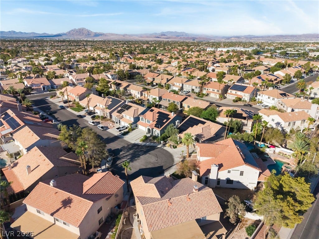 Sun-drenched tile roofs crown this quiet neighborhood under a clear sky and distant mountains.