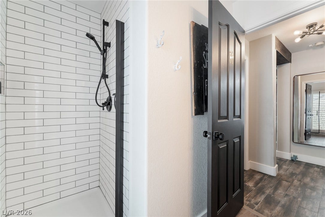 Subway tile accents the walk-in shower adjacent to a wood-look plank floor hallway.