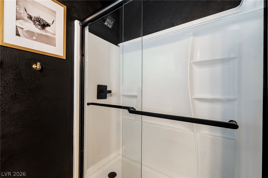 A modern walk-in shower features glass sliding doors and bold dark walls.