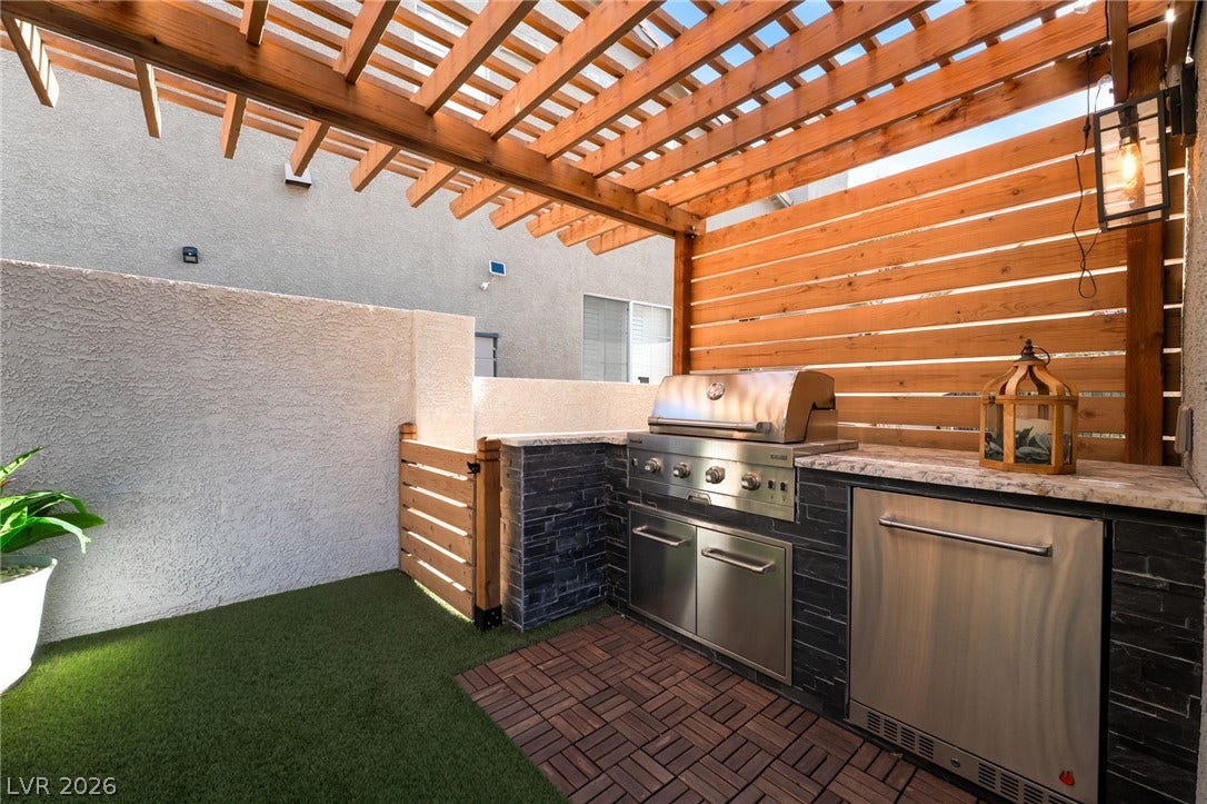 A custom wooden pergola shades this stone-finished outdoor kitchen set against a private courtyard wall.