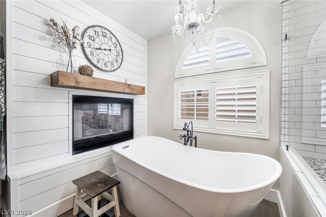 A freestanding tub sits beneath a graceful arched window adjacent to a cozy fireplace.