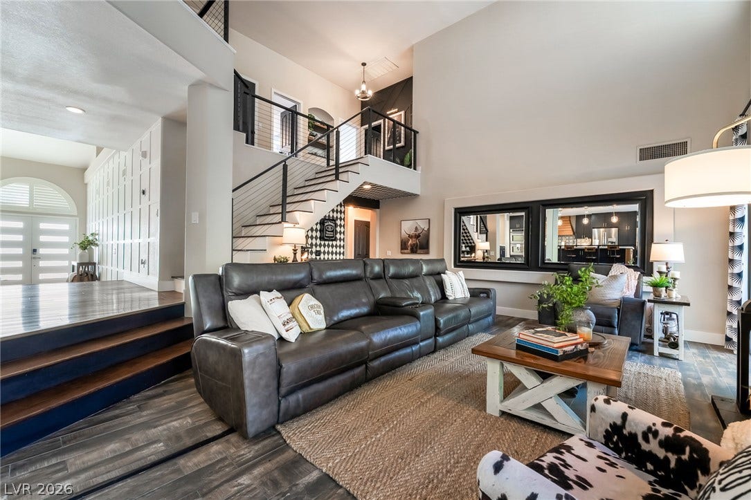 High ceilings and a modern staircase define this open living space with wood flooring.