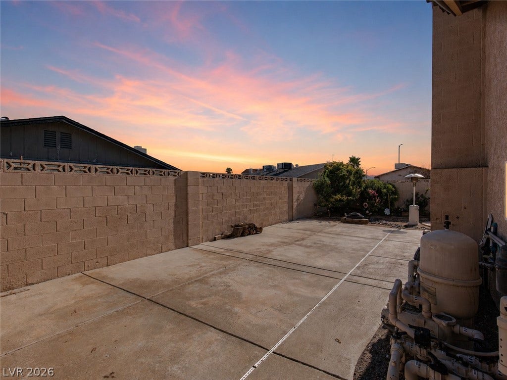 737 Brick Drive, Henderson, NV 89002 Concrete hardscaping leads to a secure perimeter wall under a dramatic sunset sky.