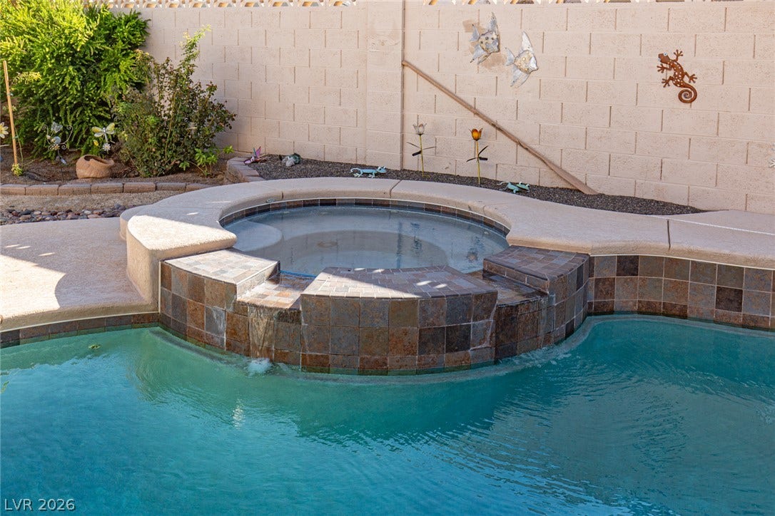 737 Brick Drive, Henderson, NV 89002 An integrated spa overflows into the pool, bordered by a concrete patio and block fencing.