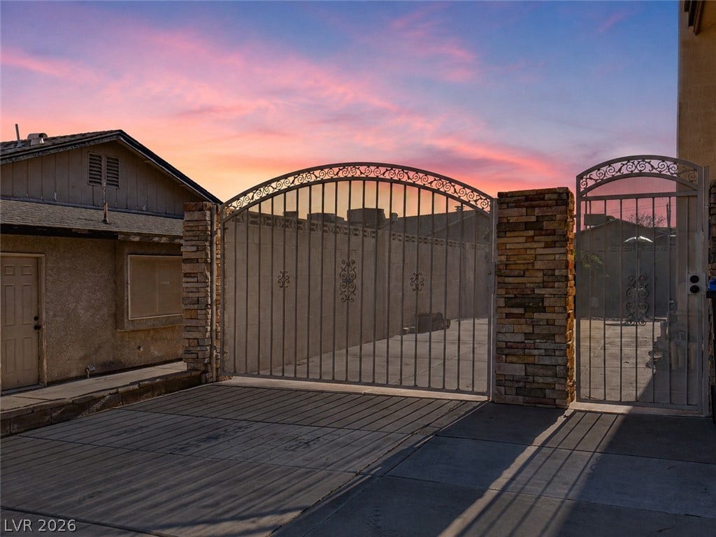 737 Brick Drive, Henderson, NV 89002 An arched wrought-iron security gate framed by stone pillars secures the driveway entry.