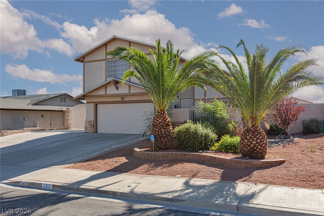 737 Brick Drive, Henderson, NV 89002 Palm trees frame the classic two-story exterior featuring a spacious concrete driveway and tiled roof accents.