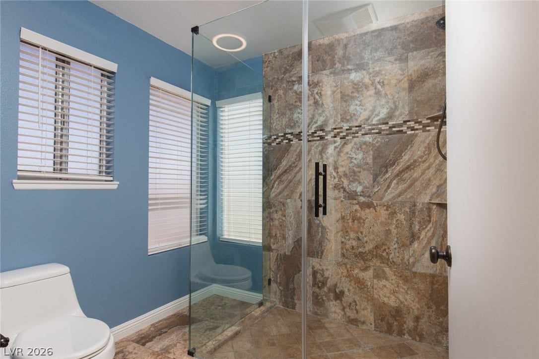 737 Brick Drive, Henderson, NV 89002 Earth-toned stone tiles line the glass-enclosed shower alongside classic wood trim.