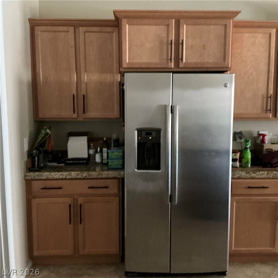 Ample wooden cabinetry and stone countertops frame a modern stainless steel refrigerator.