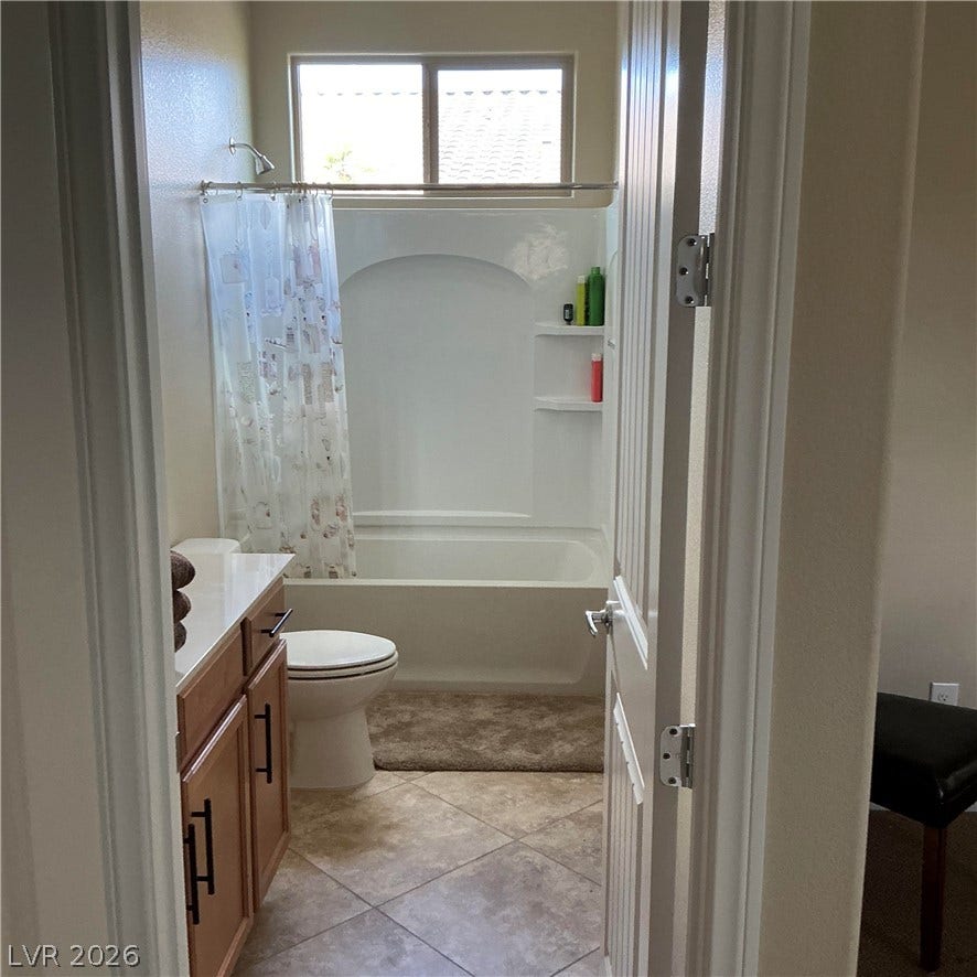 A classic tiled bathroom features a shower-tub combination and functional wood vanity.