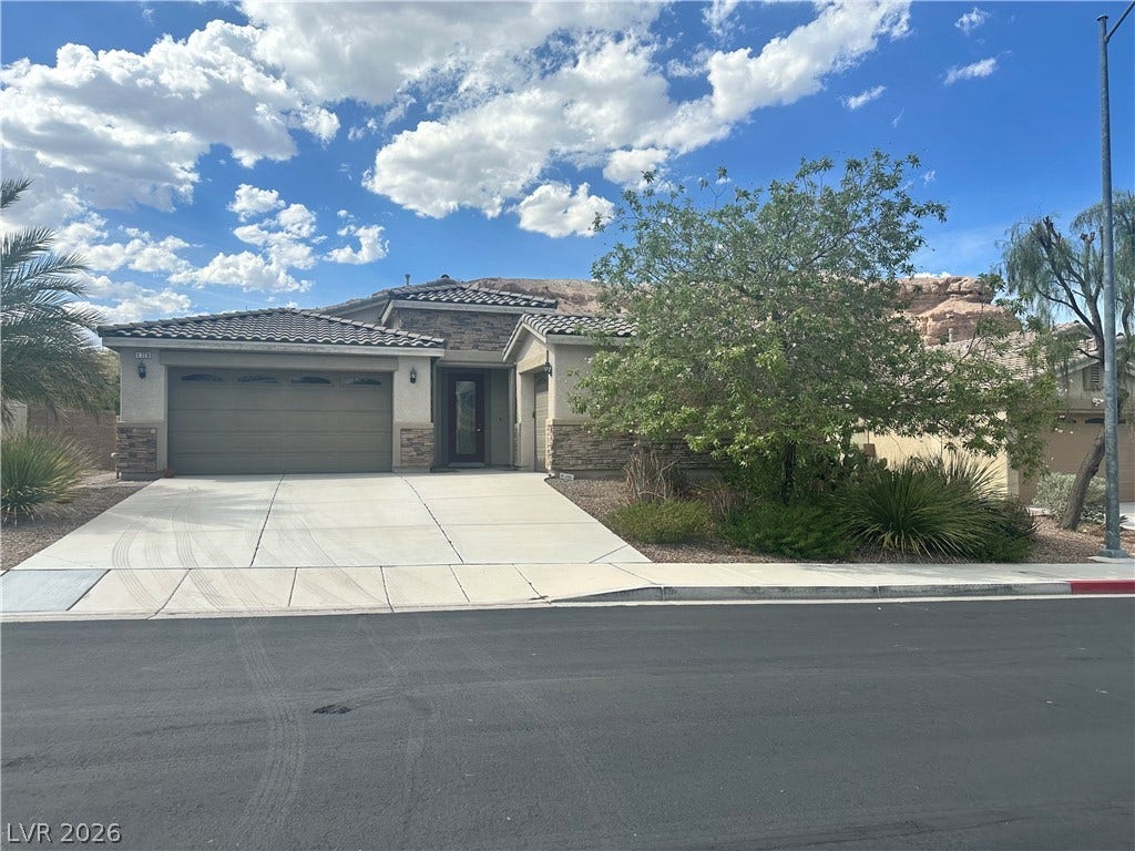 Desert landscaping and stone accents frame this contemporary stucco home beneath a wide blue sky.