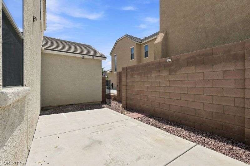 10464 Calico Pines Avenue, Las Vegas, NV 89135 A private paved courtyard path runs alongside the stucco exterior wall and a block privacy fence.