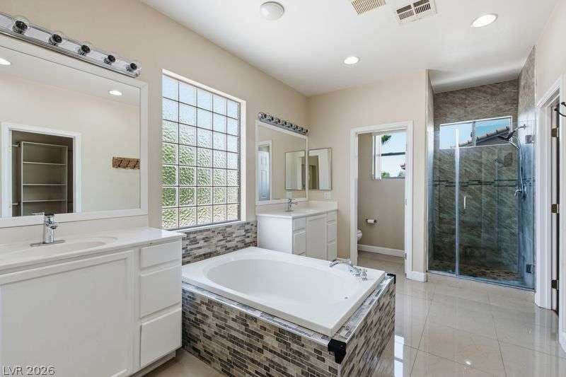 10464 Calico Pines Avenue, Las Vegas, NV 89135 A spacious bathroom features dual vanities, a tiled soaking tub, and a glass-enclosed shower.