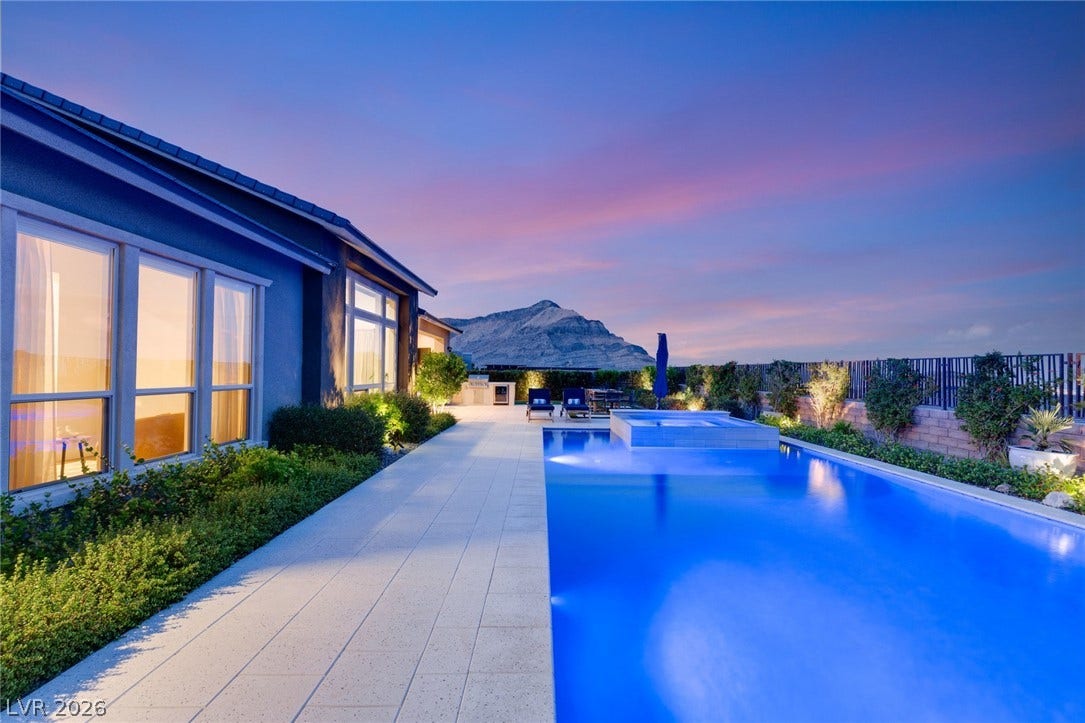 A sparkling swimming pool and integrated spa frame dramatic mountain backdrops under twilight skies.