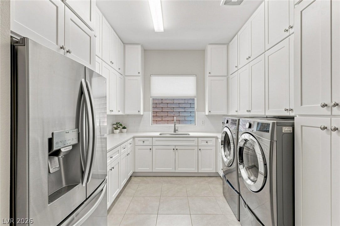 Extensive cabinetry, sink and secondary refrigerator in this highly functional laundry room.
