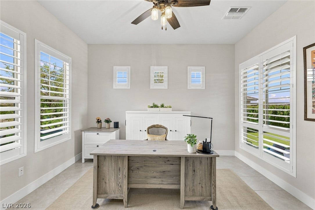 A spacious home workspace is illuminated by numerous windows equipped with classic plantation shutters.
