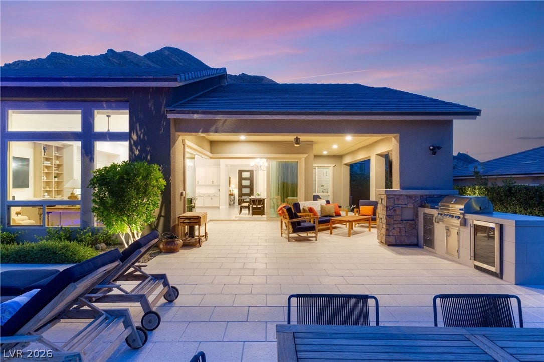 A spacious stone patio opens to an outdoor kitchen set against a mountain backdrop.