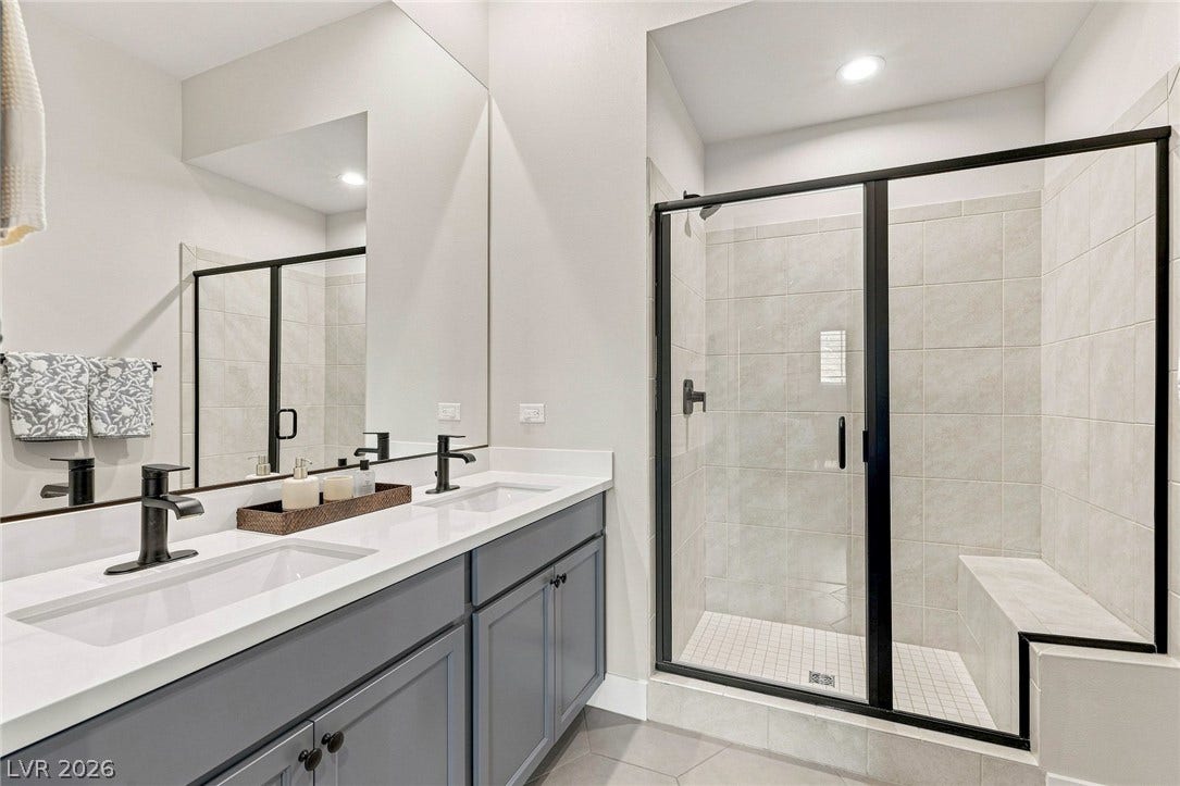 Secondary bath featuring dual sinks and shower with bench.