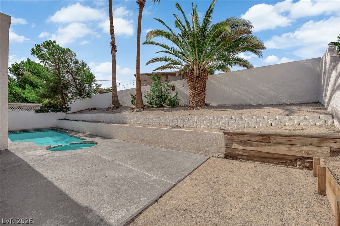 1433 Pathfinder Road, Henderson, NV 89014 A concrete patio borders the pool amidst tiered desert landscaping under a blue sky.