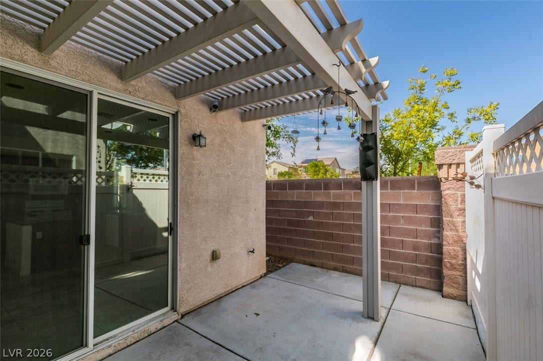 An inviting concrete patio features a protective overhead pergola and sliding glass doors.