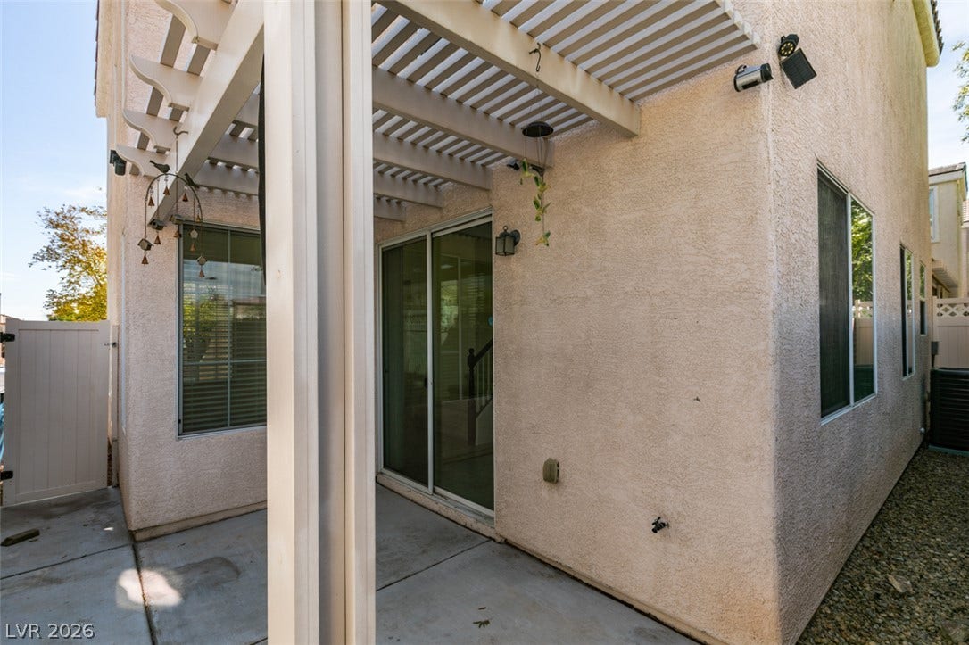 An inviting concrete patio features a white wooden pergola overhead.