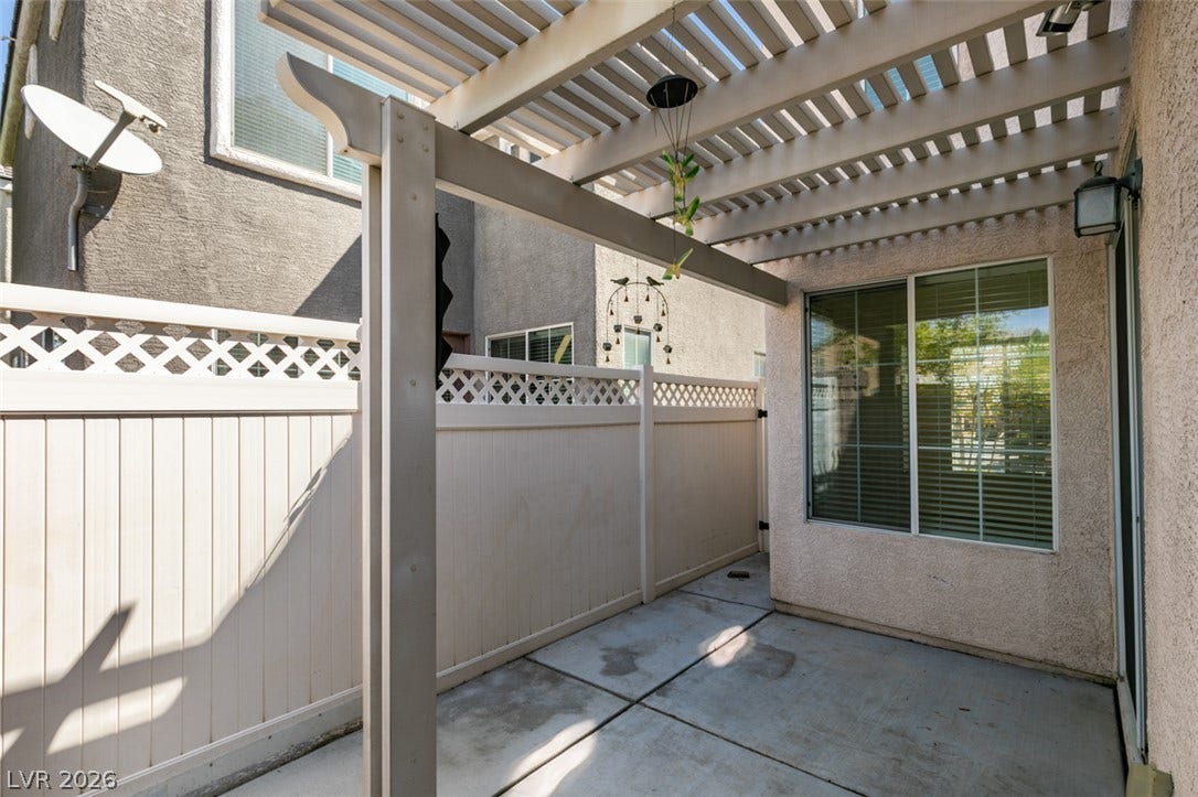 A private concrete patio sits sheltered beneath a classic wooden pergola structure.