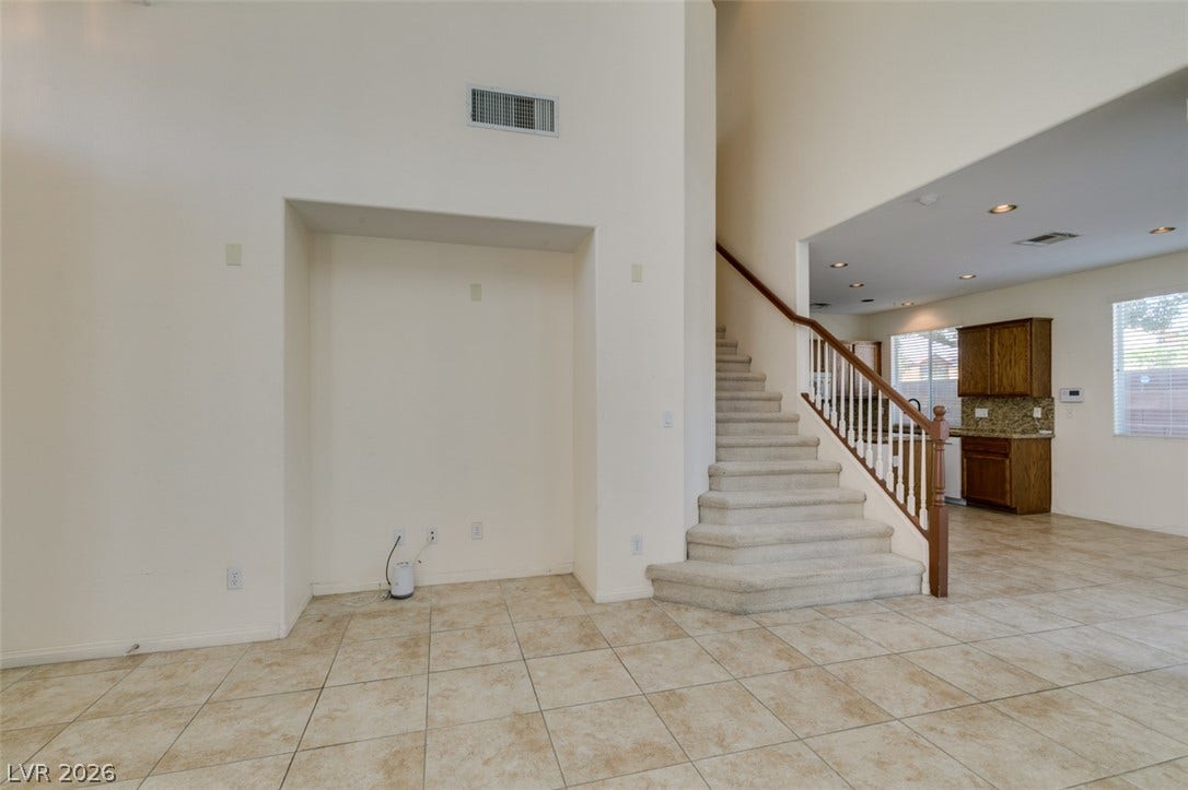 Tiled flooring and high ceilings define this open entry showcasing a carpeted staircase.