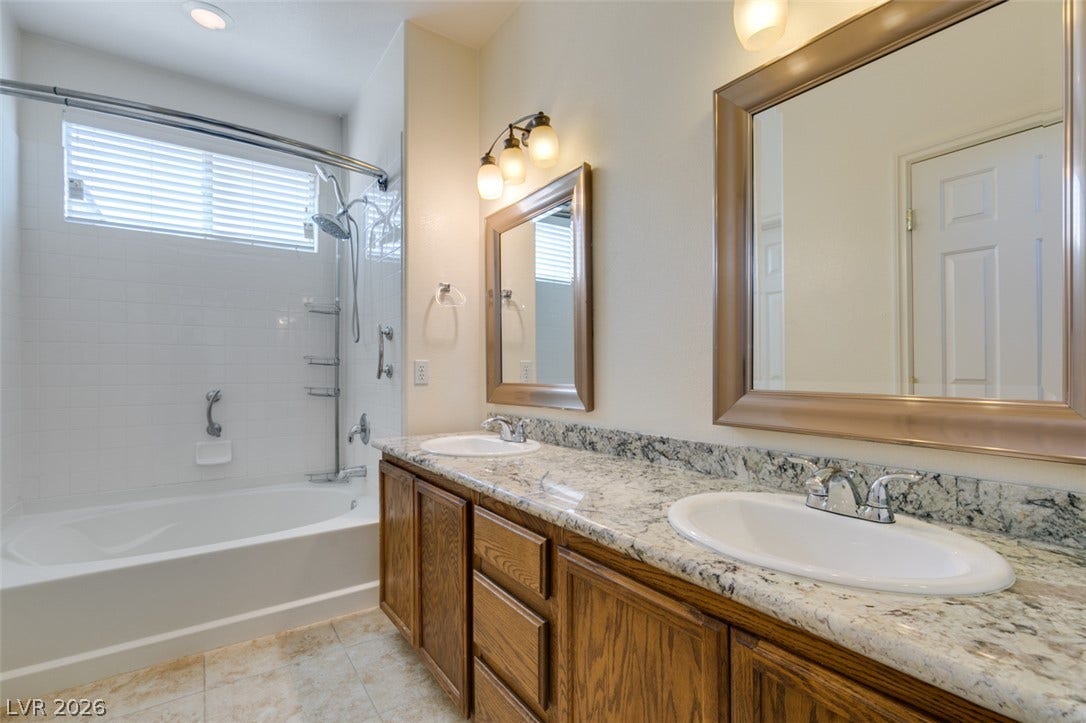 Polished granite countertops complement the double vanity alongside a tiled tub and shower combination.