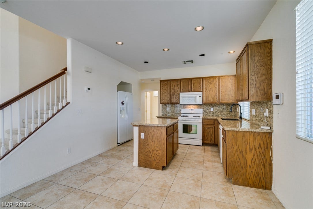 An open kitchen layout incorporates tiled flooring, wooden cabinetry, and granite countertops.