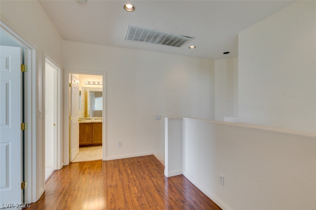 Rich wood flooring anchors this upper level hallway opening to adjacent rooms.