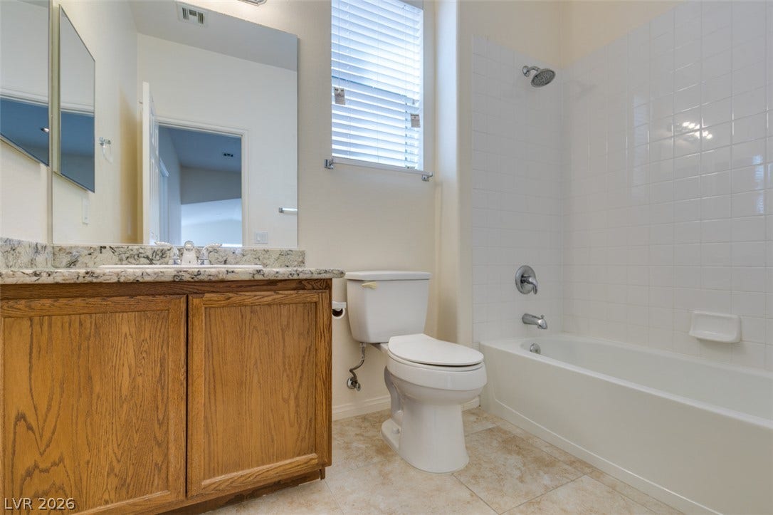 Tiled flooring and a stone-topped vanity define this functional full bathroom.