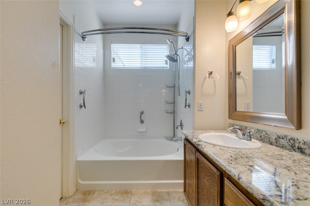 Polished stone countertops and a tiled tub-and-shower alcove define this practical bathroom design.