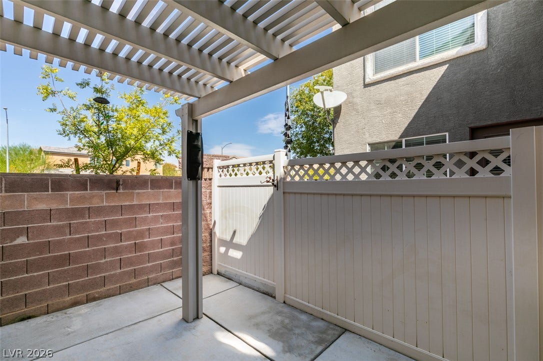 An inviting concrete patio features a protective overhead pergola and private fencing.