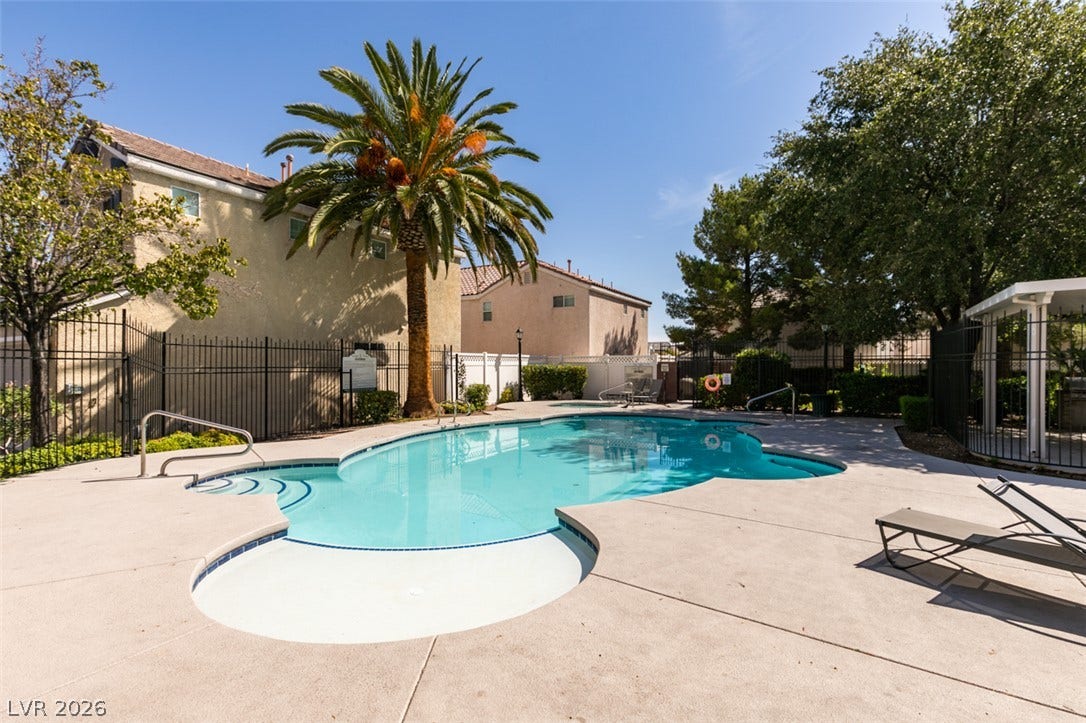 A sparkling swimming pool surrounded by a spacious concrete patio and security fencing.